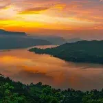 a breathtaking sunset casts vibrant orange and pink hues over a tranquil lake, reflecting the colors of the sky and surrounding lush greenery, creating a serene atmosphere of nature's beauty.